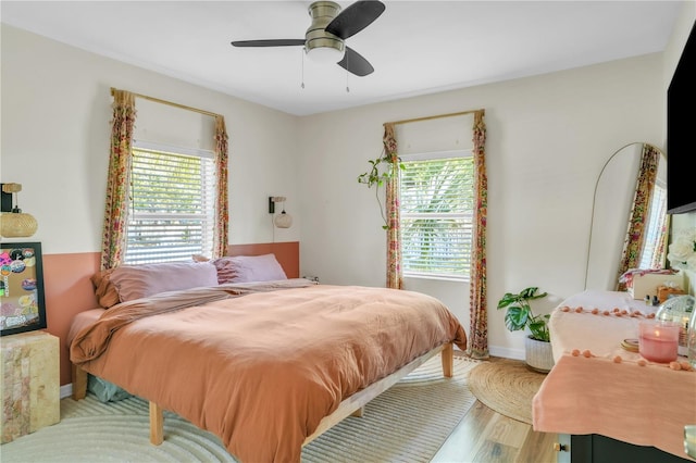 bedroom with baseboards, multiple windows, ceiling fan, and wood finished floors
