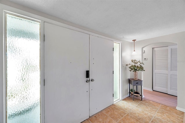 entryway with light tile patterned floors, arched walkways, and a textured ceiling