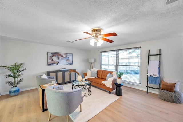living area with baseboards, a textured ceiling, light wood-style flooring, and ceiling fan