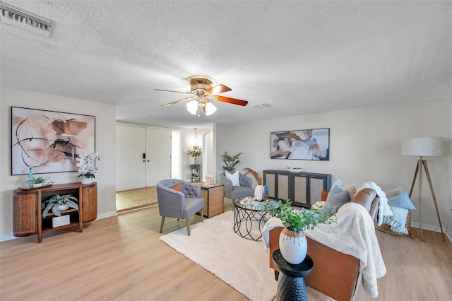 living room with a textured ceiling, light wood-style flooring, a ceiling fan, baseboards, and visible vents