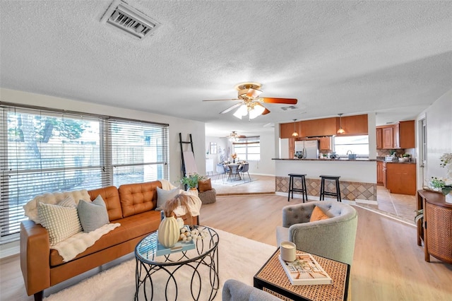 living room featuring visible vents, a textured ceiling, light wood-style flooring, and ceiling fan