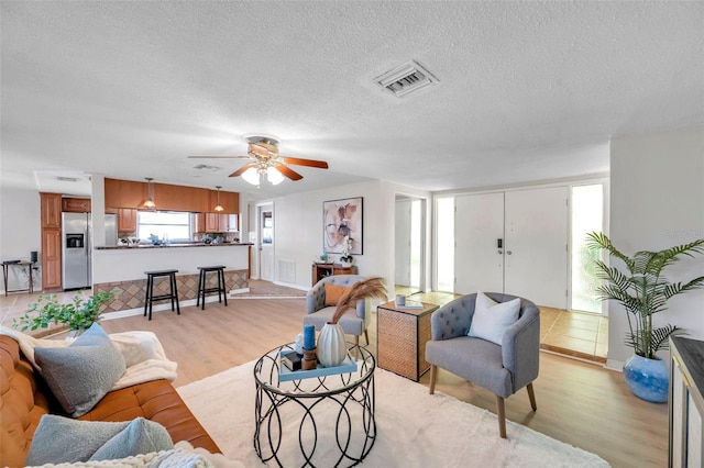 living room featuring a ceiling fan, a textured ceiling, visible vents, and light wood finished floors