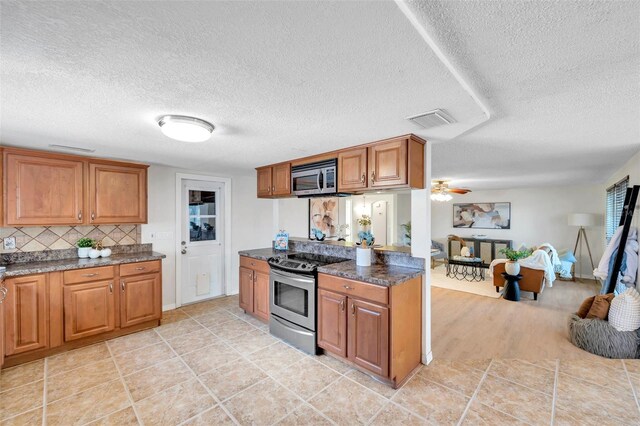 kitchen with appliances with stainless steel finishes, brown cabinets, a textured ceiling, and visible vents