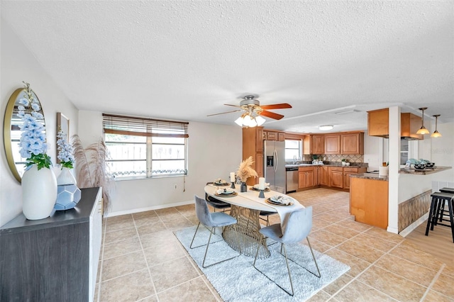 dining space featuring baseboards, a ceiling fan, light tile patterned flooring, and a textured ceiling