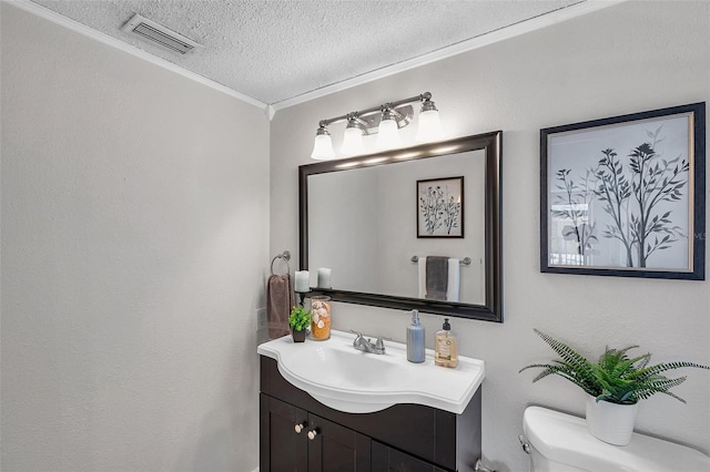 bathroom featuring visible vents, crown molding, vanity, toilet, and a textured ceiling