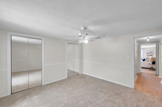 unfurnished bedroom featuring carpet flooring, a textured ceiling, two closets, a ceiling fan, and visible vents