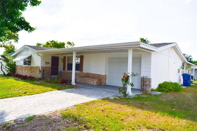 view of front of home featuring a front yard, an attached garage, stone siding, covered porch, and driveway
