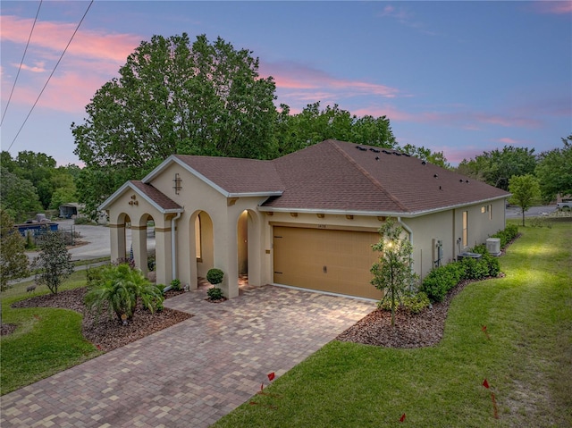 mediterranean / spanish-style home featuring driveway, roof with shingles, stucco siding, an attached garage, and a yard
