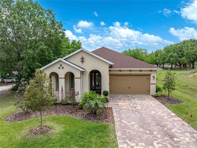 mediterranean / spanish-style house with decorative driveway, an attached garage, a front lawn, roof with shingles, and stucco siding