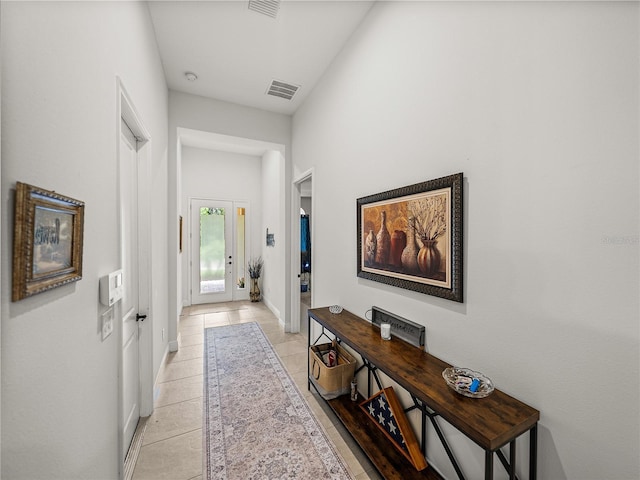 hall featuring baseboards, visible vents, and light tile patterned floors