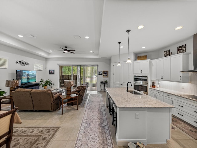 kitchen with a tray ceiling, a sink, stainless steel double oven, open floor plan, and ceiling fan
