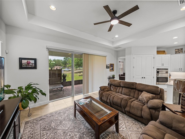 living room featuring a tray ceiling, recessed lighting, light tile patterned floors, baseboards, and ceiling fan