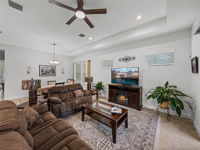 living room with a tray ceiling, ceiling fan with notable chandelier, visible vents, and recessed lighting