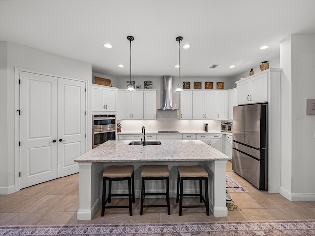 kitchen featuring wall chimney exhaust hood, white cabinetry, a sink, and stainless steel appliances