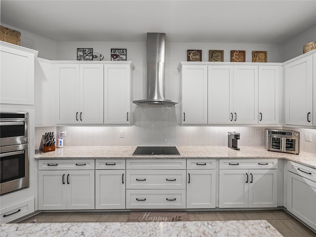 kitchen with decorative backsplash, black electric cooktop, stainless steel double oven, white cabinetry, and wall chimney range hood
