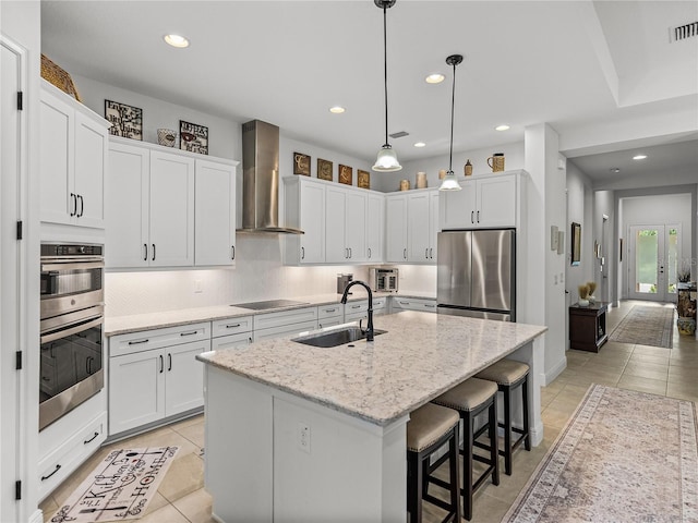 kitchen with backsplash, a center island with sink, a sink, appliances with stainless steel finishes, and wall chimney exhaust hood
