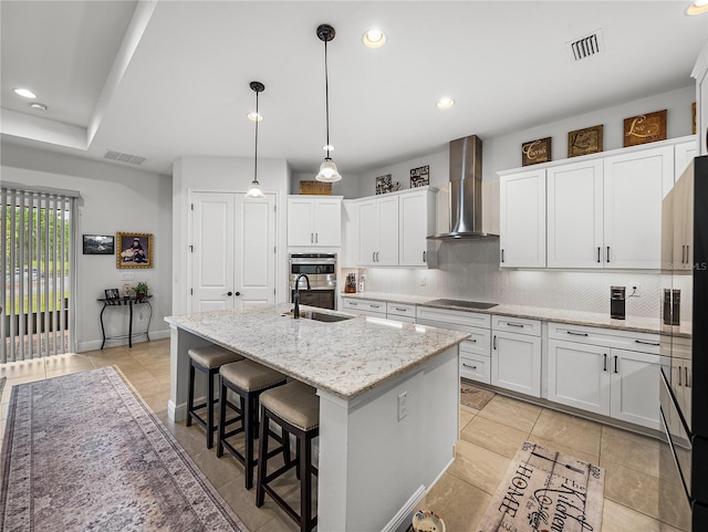 kitchen featuring wall chimney range hood, visible vents, black electric stovetop, and a sink