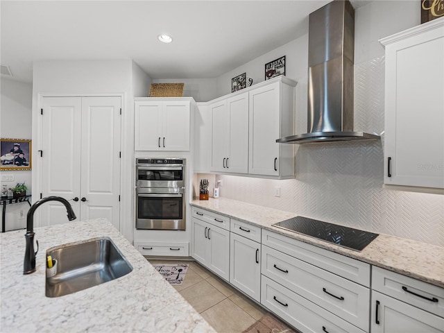 kitchen featuring a sink, double oven, wall chimney exhaust hood, tasteful backsplash, and black electric stovetop