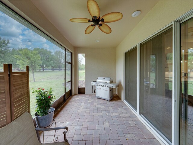 unfurnished sunroom featuring ceiling fan and brick floor