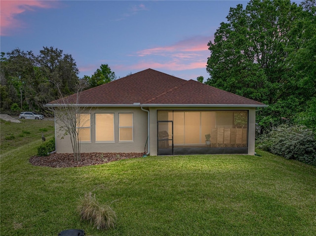 rear view of house with a shingled roof, stucco siding, a sunroom, and a yard