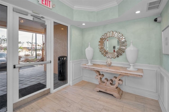 entryway with crown molding, a wainscoted wall, visible vents, and a decorative wall