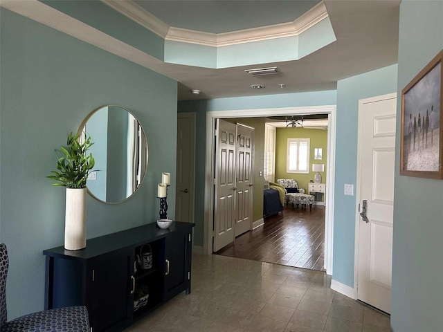 foyer entrance with a tray ceiling, visible vents, baseboards, and ornamental molding