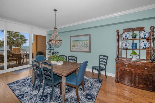 dining space with light wood-type flooring, crown molding, baseboards, and a notable chandelier