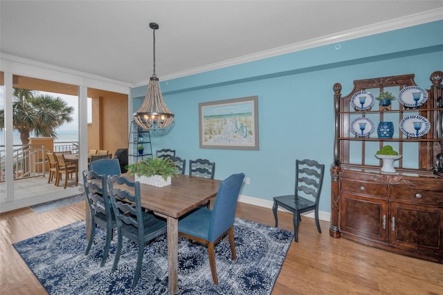 dining space with baseboards, a notable chandelier, crown molding, and light wood-type flooring