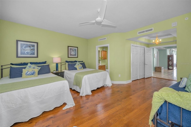 bedroom with ensuite bath, wood finished floors, visible vents, and ceiling fan with notable chandelier