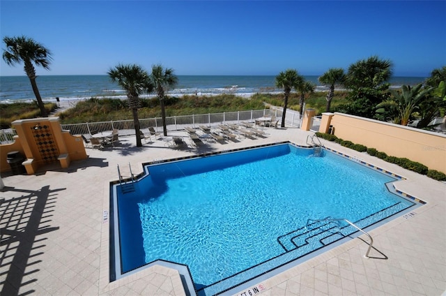 community pool with fence, a patio, and a water view