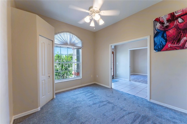 carpeted spare room featuring tile patterned floors, baseboards, and a ceiling fan