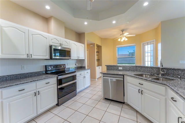 kitchen featuring a sink, decorative backsplash, dark stone countertops, stainless steel appliances, and ceiling fan