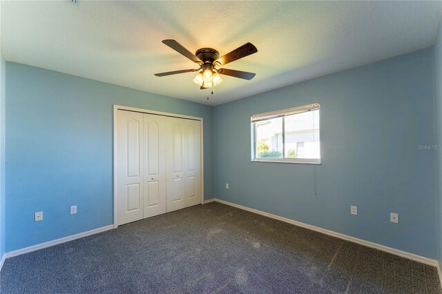 unfurnished bedroom with baseboards, a closet, dark colored carpet, and ceiling fan