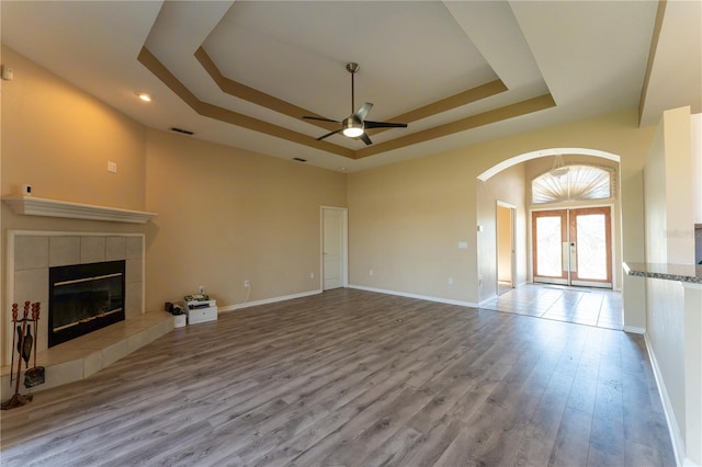 unfurnished living room with visible vents, ceiling fan, wood finished floors, arched walkways, and a tray ceiling