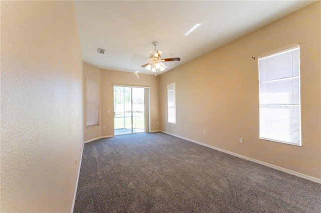 empty room featuring baseboards, visible vents, dark carpet, and a ceiling fan