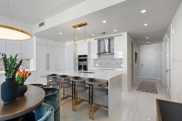 kitchen with visible vents, modern cabinets, stainless steel double oven, white cabinetry, and wall chimney range hood