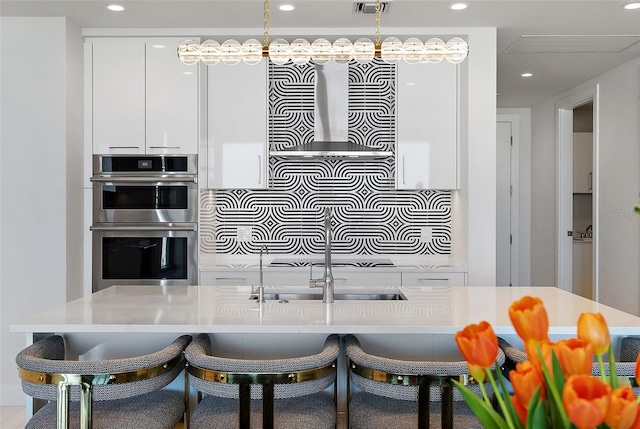 kitchen featuring a sink, white cabinetry, double oven, a breakfast bar area, and modern cabinets