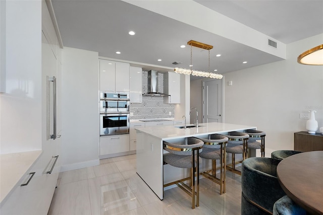 kitchen featuring a sink, tasteful backsplash, a kitchen breakfast bar, modern cabinets, and wall chimney range hood