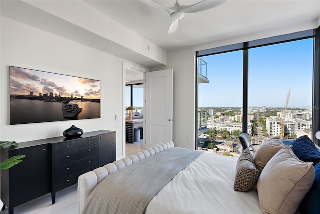 bedroom featuring floor to ceiling windows, ceiling fan, a view of city, and light wood finished floors