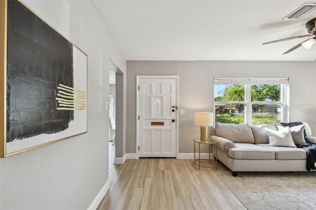 living room with light wood-type flooring, baseboards, ceiling fan, and visible vents