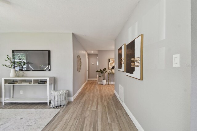 hall featuring baseboards, visible vents, and wood finished floors