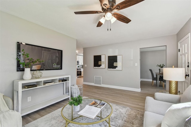 living room with baseboards, visible vents, wood finished floors, and ceiling fan