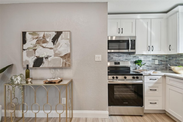 kitchen with decorative backsplash, white cabinets, light wood-style flooring, and appliances with stainless steel finishes