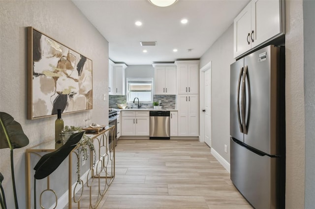 kitchen with white cabinetry, light countertops, stainless steel appliances, backsplash, and a sink