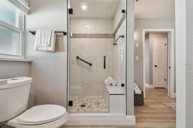 bathroom with baseboards, toilet, a stall shower, and wood finished floors