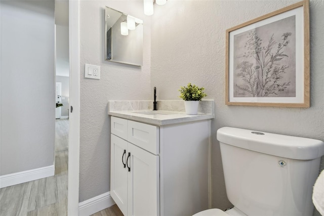 bathroom featuring baseboards, toilet, wood finished floors, vanity, and a textured wall