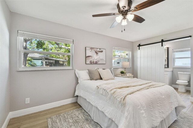 bedroom with baseboards, a barn door, ceiling fan, and wood finished floors