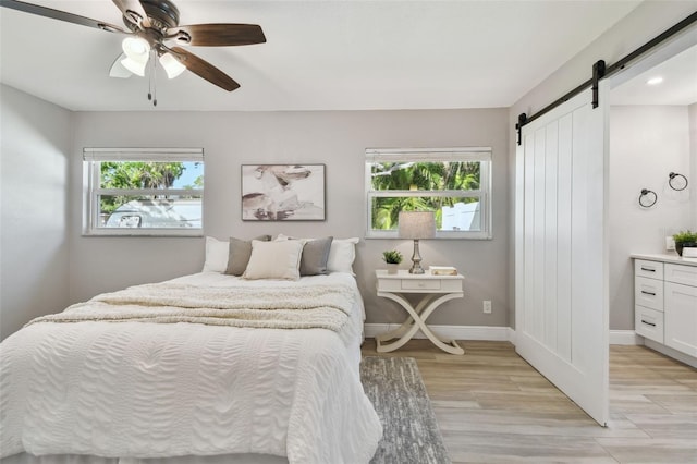 bedroom with multiple windows, baseboards, a barn door, and light wood-type flooring