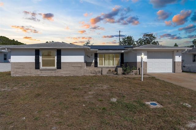 ranch-style home featuring driveway, a garage, stucco siding, solar panels, and a lawn