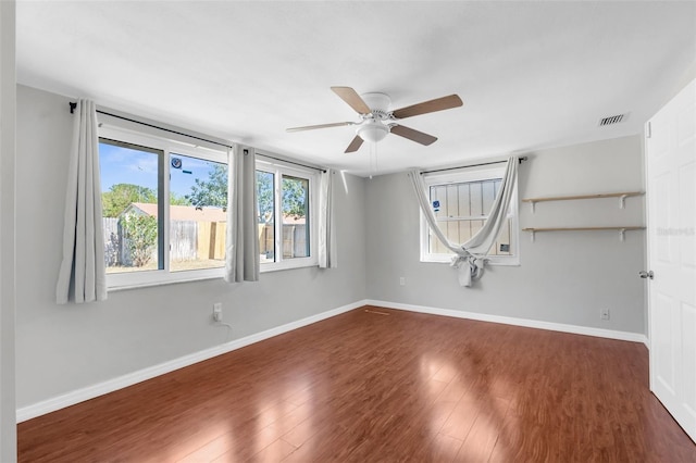 empty room with dark wood finished floors, baseboards, ceiling fan, and visible vents